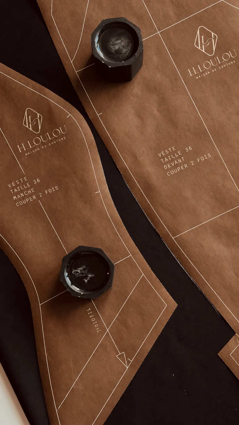 Illustrative paper pattern pieces carrying the H·LOULOU mark, held by weights